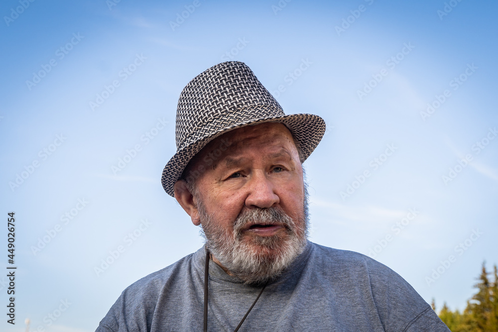 Wise old sad man with blue eyes. Senior aged caucasian white man dressed in hat. Portrait of an elderly man disabled pensioner. Rehabilitation of disabled people. Person male at summer day.