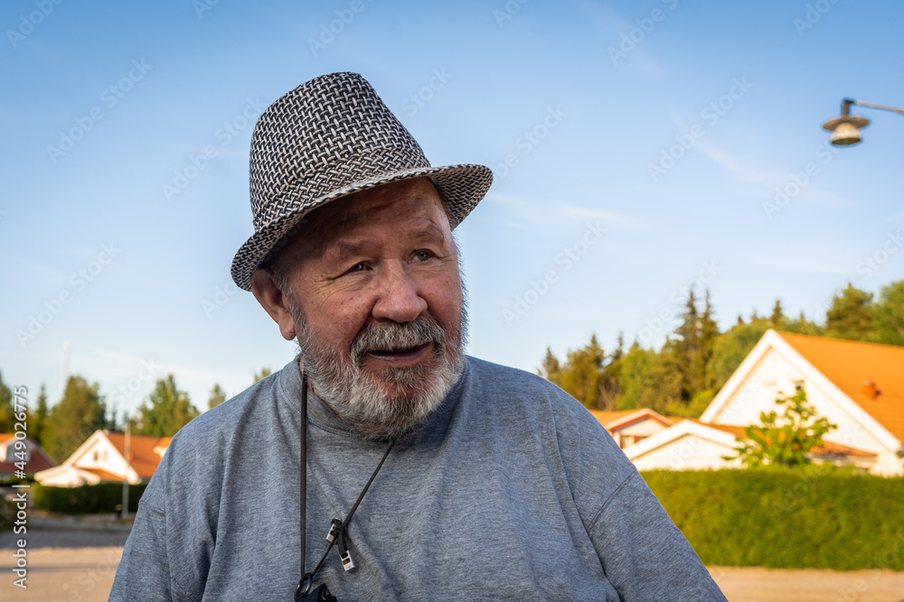 Wise old sad man with blue eyes. Senior aged caucasian white man dressed in hat. Portrait of an elderly man disabled pensioner. Rehabilitation of disabled people. Person male at summer day.