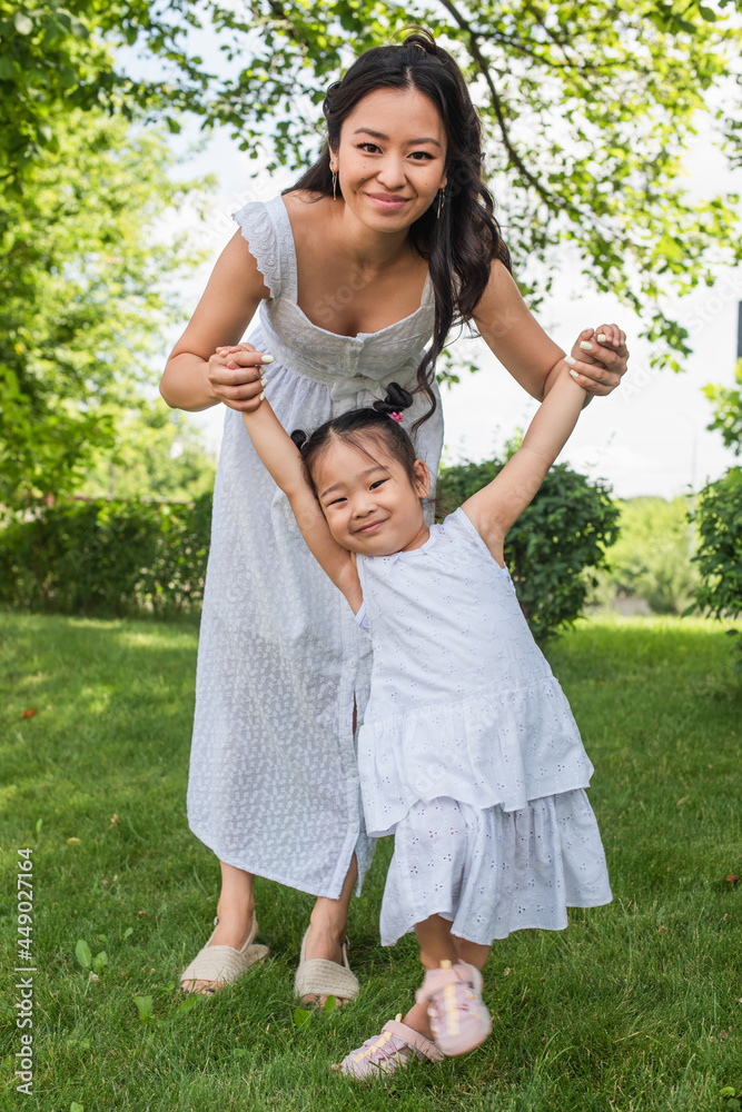 happy mother and toddler asian kid in dresses holding hands in park happy mother and toddler asian kid in dresses holding hands in park