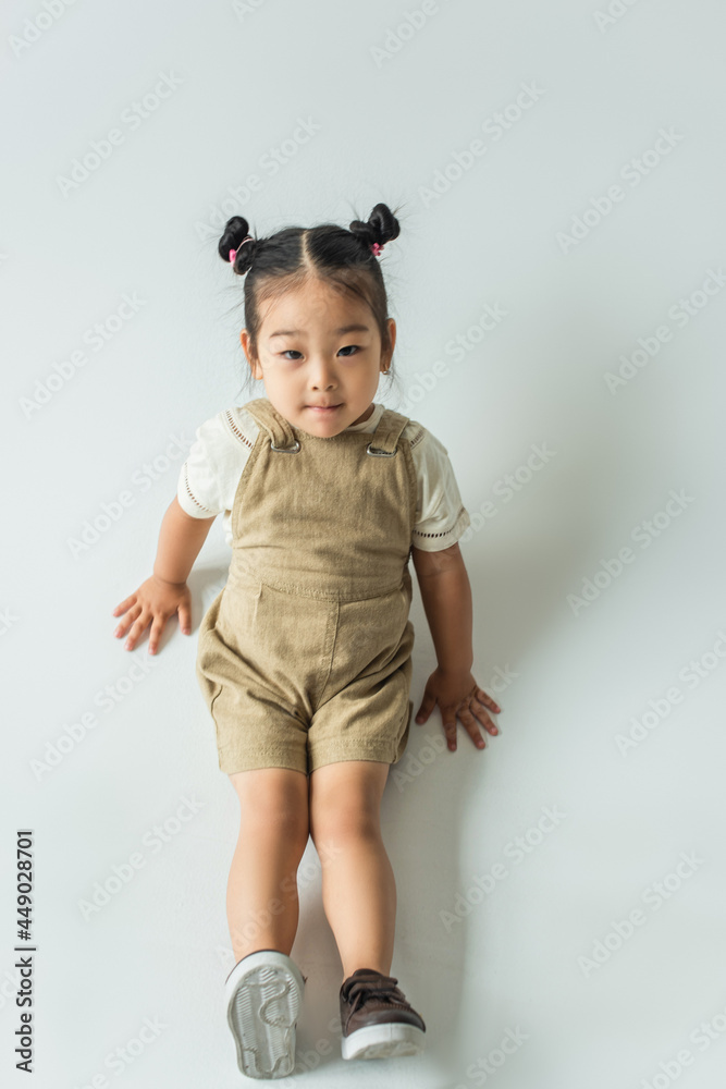 high angle view of asian toddler kid posing while sitting on grey high angle view of asian toddler kid posing while sitting on grey