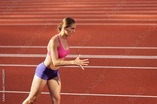 One Caucasian woman, female athlete, runner training at public stadium, sport court or palyground outdoors. Summer sport games. © master1305