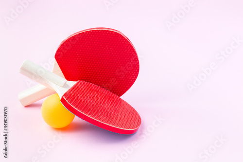 Children mini rackets ping pong or table tennis and orange ball on pink background, horizontal, copy space
