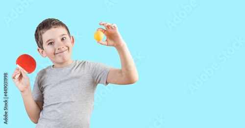 Cute nine years old boy in a gray t-shirt with mini table tennis racket and orange ball. Mini ping pong table game