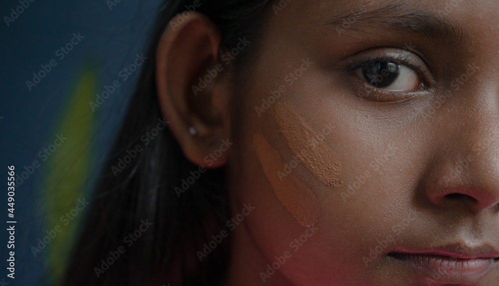 Extreme close up of a dark-skinned face of a young girl with cosmetic foundation strokes applied on healthy skin