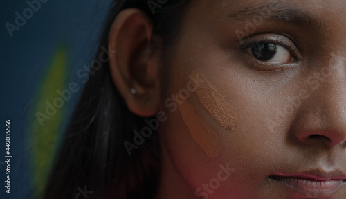 Extreme close up of a dark-skinned face of a young girl with cosmetic foundation strokes applied on healthy skin