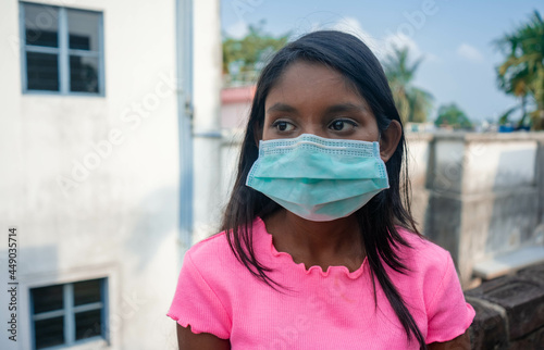Image of a young dark-skinned teenage girl looking in despair, wearing a protective medical mask outdoors for air pollution, dust allergies, and spreading disease and viruses | Concept of COVID