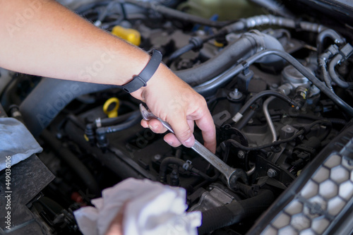Auto mechanic working repairing a car engine with an open-end spanner in a garage