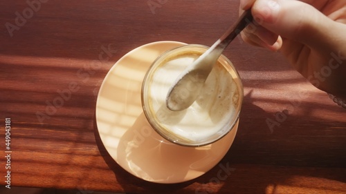 Elegant female hand stirring affogato coffee with a wooden spoon. Delicious morning caffeine drink for a woman. Avogato in the golden light through shutters on a wooden table. Lady enjoying beverage. photo