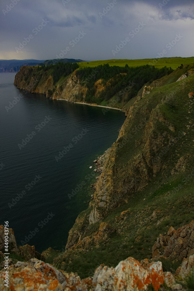 Clouds are gathering over the steep shores of Olkhon Island. The dark water of Lake Baikal on a cloudy day. A beautiful dark background. A summer landscape in Siberia. The harsh nature of Siberia.