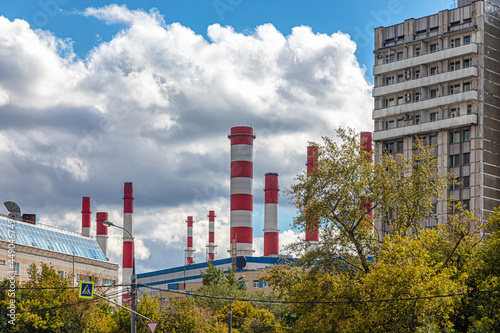 Large and tall white-red pipes of a thermal power plant against a cloudy sky