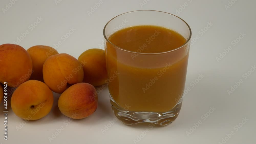 Glass cup with an apricot juice with a pulp, the ripe apricots are on a white table Glass cup with an apricot juice with a pulp, the ripe apricots are on a white table