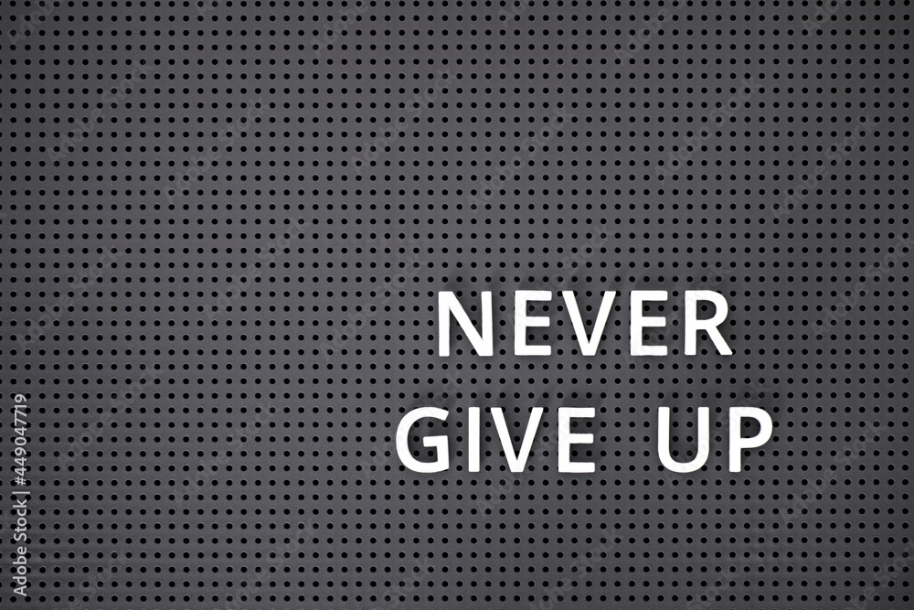 Phrase Never Give Up spelled out with white letters on gray pegboard Phrase Never Give Up spelled out with white letters on gray pegboard
