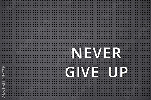 Phrase Never Give Up spelled out with white letters on gray pegboard photo