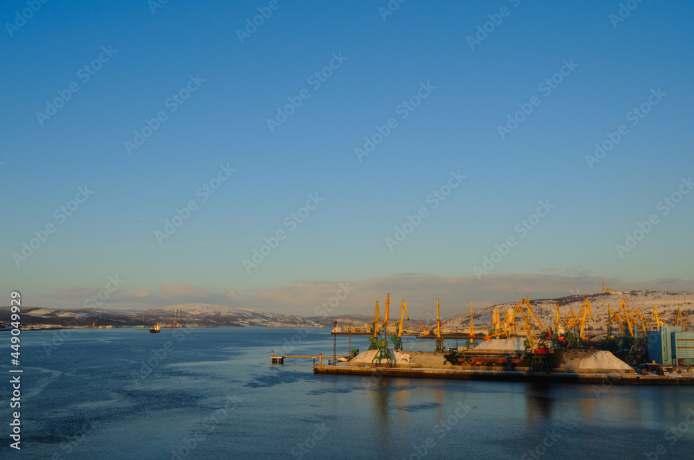 Murmansk, Russia-November 2010: Murmansk Commercial Sea Port. Tall yellow cranes against the backdrop of snow-capped mountains and the monument to Alyosha. Kola Bay.