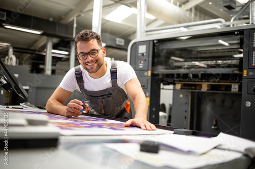 Print house worker controlling printing process quality and checking colors with magnifying glass.