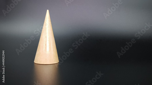the triangular cone is made of wood on a black background. various geometric shapes are trending