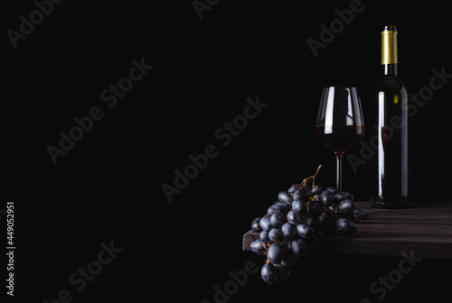 A glass of red wine, a bottle and grapes on a dark background. Free space for text. Alcoholic beverage