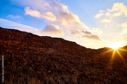 Nature landscape with golden hills, sun, blue sky with yellow clouds in a day or a evening during sunset