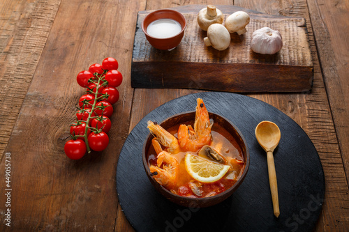 Tom yam soup with shrimps and coconut milk on the table on a round board near milk mushrooms and tomatoes.