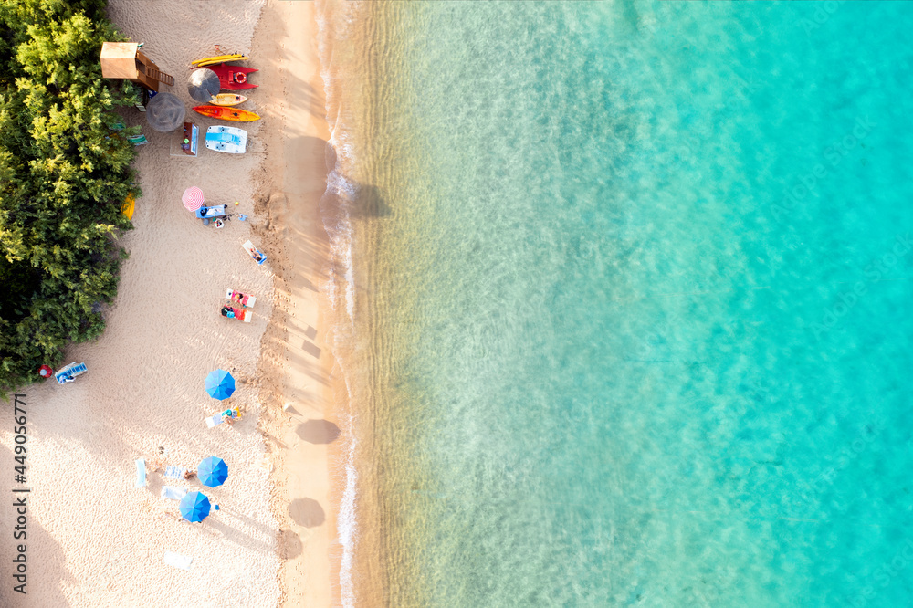 View from above, stunning aerial view of a white sand beach bathed by a turquoise water and relaxed people under some beach umbrellas at sunset. Cala di volpe beach,Sardinia, Italy.