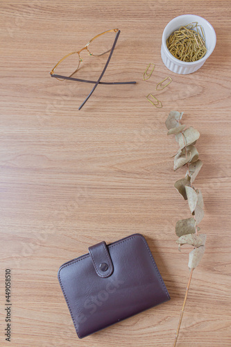 Minimalist office desk workspace with glasses, wallet, dried eucalyptus branch, golden paper clips on a wooden background. Flat lay, top view. Finances concept.