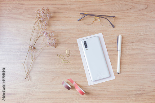 Workspace with smatphone, glasses, wildflower, pen, washi tapes and paper clips on wooden background. Flat lay, top view