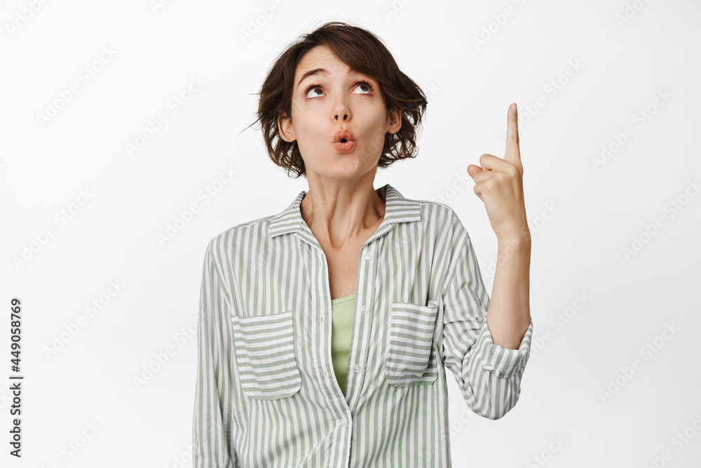 Wow look at that. Excited girl pointing, looking up with amazed face expression, showing advertisement, store website, standing over white background Wow look at that. Excited girl pointing, looking up with amazed face expression, showing advertisement, store website, standing over white background