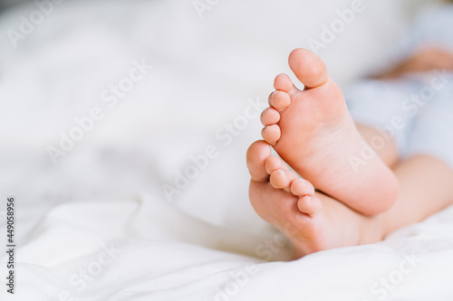 Close up barefoot baby feet lying on white bed linen. Fabric softener, cleanliness. Space for message