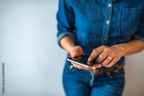 Cropped image of happy girl using smartphone device. Woman in casuals standing in office by a window with phone in hand. Businesswoman with mobile phone in hand.