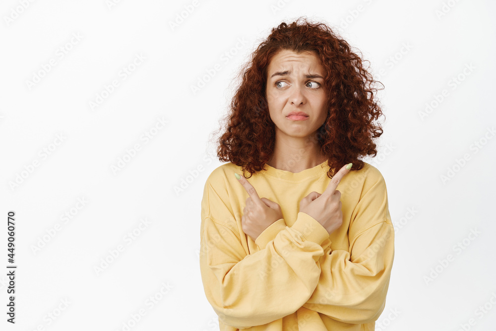 Image of indecisive girl has trouble with choosing, pointing sideways and looking left with confused face expression, white background Image of indecisive girl has trouble with choosing, pointing sideways and looking left with confused face expression, white background