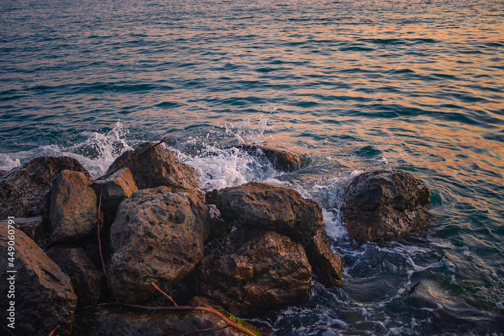 Obraz premium Orange sunset on the beach with big stones. Sunset on a rocky stone beach. Large stones with a beautiful texture against the background of a sea sunset. Evening landscape on the rocky sea shore.
