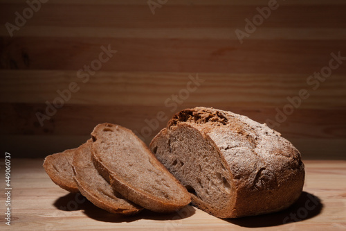 Fresh handmade wheat bread cut into pieces on wooden background in the contrast light. horizontal frame side view with space area for text or design