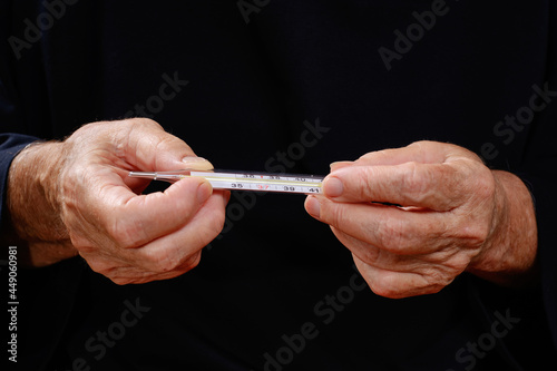 Close up of hands elderly woman holding thermometer. Selective focus on hands wrinkled skin.