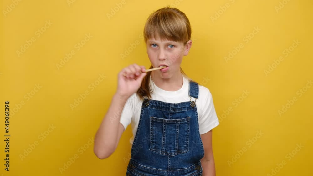Portrait cute beautiful school girl kid with long blonde hair cleaning teeth with toothbrush, looking at camera, posing isolated over yellow color background wall in studio. Dental hygiene concept Portrait cute beautiful school girl kid with long blonde hair cleaning teeth with toothbrush, looking at camera, posing isolated over yellow color background wall in studio. Dental hygiene concept