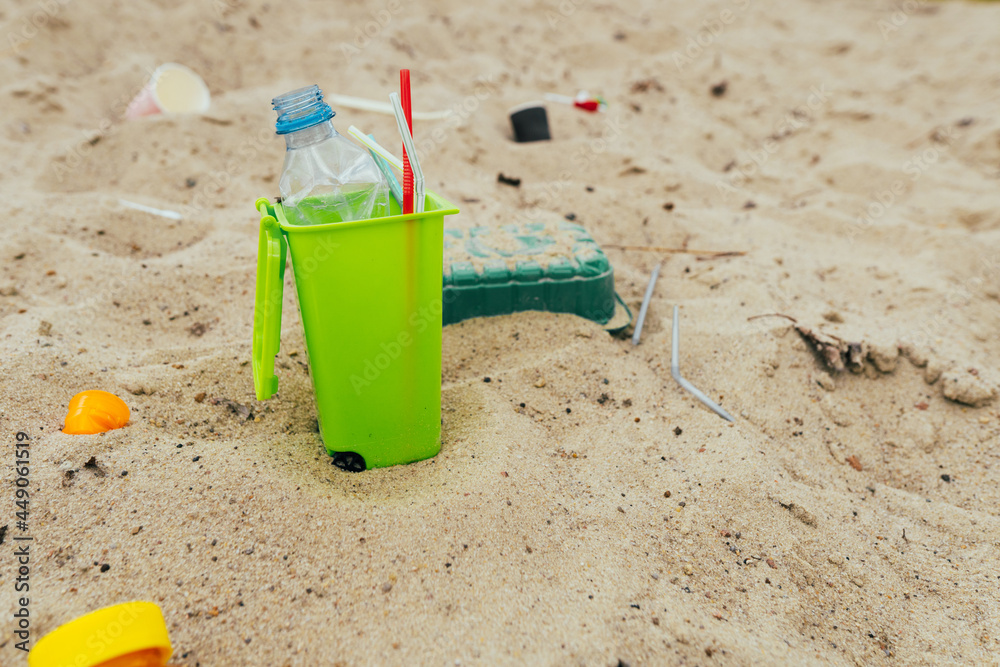Small toy waste container on the sand beach with plastic garbage Small toy waste container on the sand beach with plastic garbage