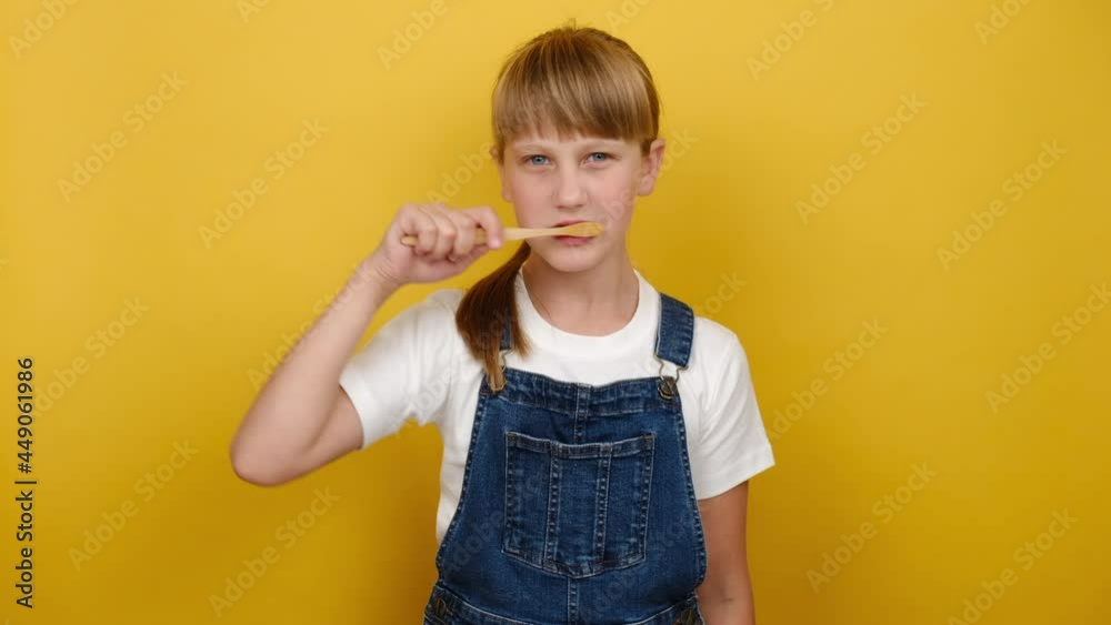 Oral health awareness concept. Portrait cute little caucasian blonde girl brush teeth, happy looking at camera, isolated over yellow color background in studio with copy space for promotion content Oral health awareness concept. Portrait cute little caucasian blonde girl brush teeth, happy looking at camera, isolated over yellow color background in studio with copy space for promotion content