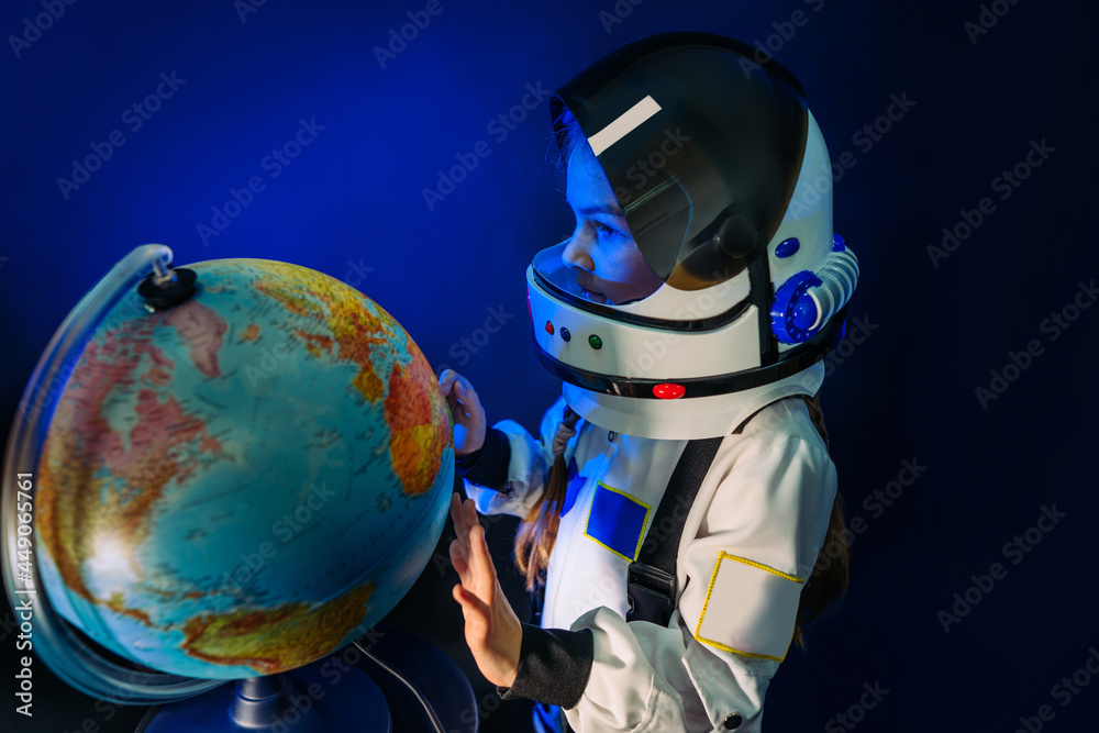Naklejka premium Teenager girl wearing astronaut costume and helmet studying the Earth globe