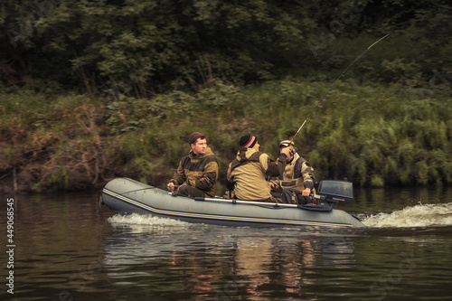 Fishermen sailing on inflatable motor boat along river bank and fishing with fishing rods 
