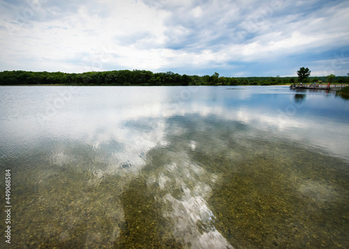 Looking out across a clear lake in Waukesha County, Wisconsin.  Fishing pier in the distance.  Clouds are reflected in the clear water. photo