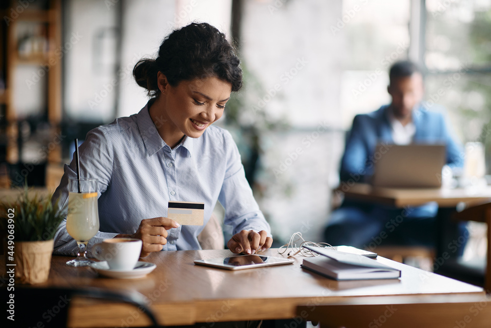 Happy businesswoman uses credit card and touchpad while shopping online at cafe. Happy businesswoman uses credit card and touchpad while shopping online at cafe.