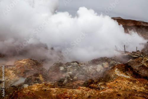 Geyser steam above broken house and the orange ground clay at geothermal area in Iceland.