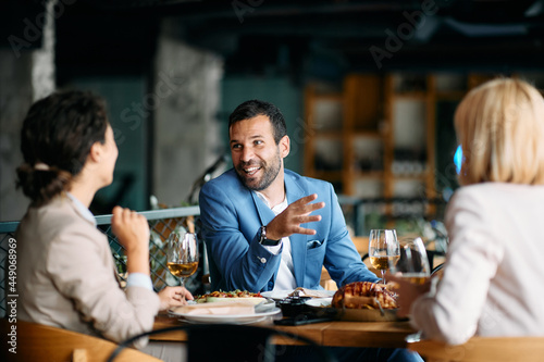 Happy entrepreneur talks to female co-workers while having business lunch at restaurant. photo