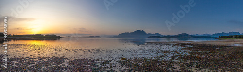 Panoramic view from beach of the setting sun on Amnesvika bay with mountains on the horizon. Island Amnoya. Norway