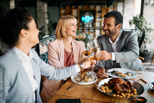 Cheerful business colleagues toast with wine during lunch in restaurant.