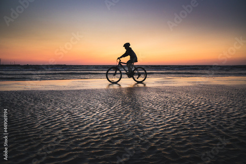Silhouette of a boy on a bicycle riding on a small portion of sand in the middle of the water from the baltic sea. Dramatic stunning sunset colors. Estonia, Europe