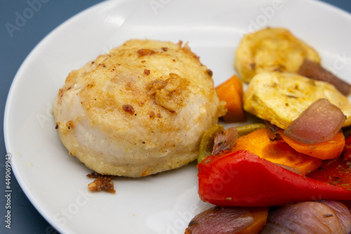 A piece of fried hake fish fillet with stewed vegetables