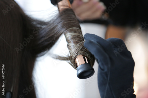 Fixing a woman s beautiful  blonde hair with a black curling iron.