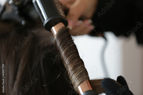 Fixing a woman s beautiful  blonde hair with a black curling iron.