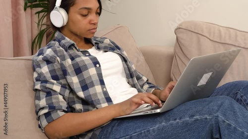 A young woman works at home online and listens to music in large white headphones. The concept of freelancing.