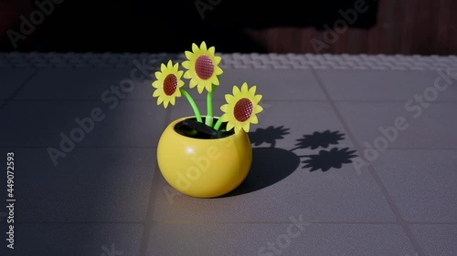 View on a solar powered plastic artificial sunflower moving by the sunlight representing renewable energy source on a table in the garden.
